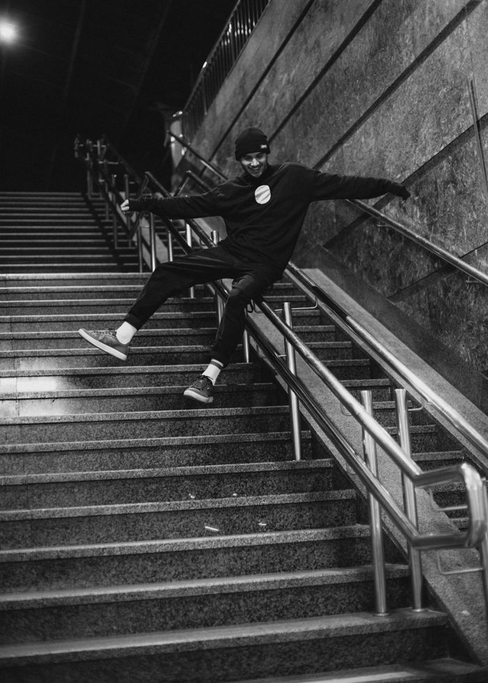 Man dynamically sliding down stairs indoors in a dramatic black-and-white setting.
