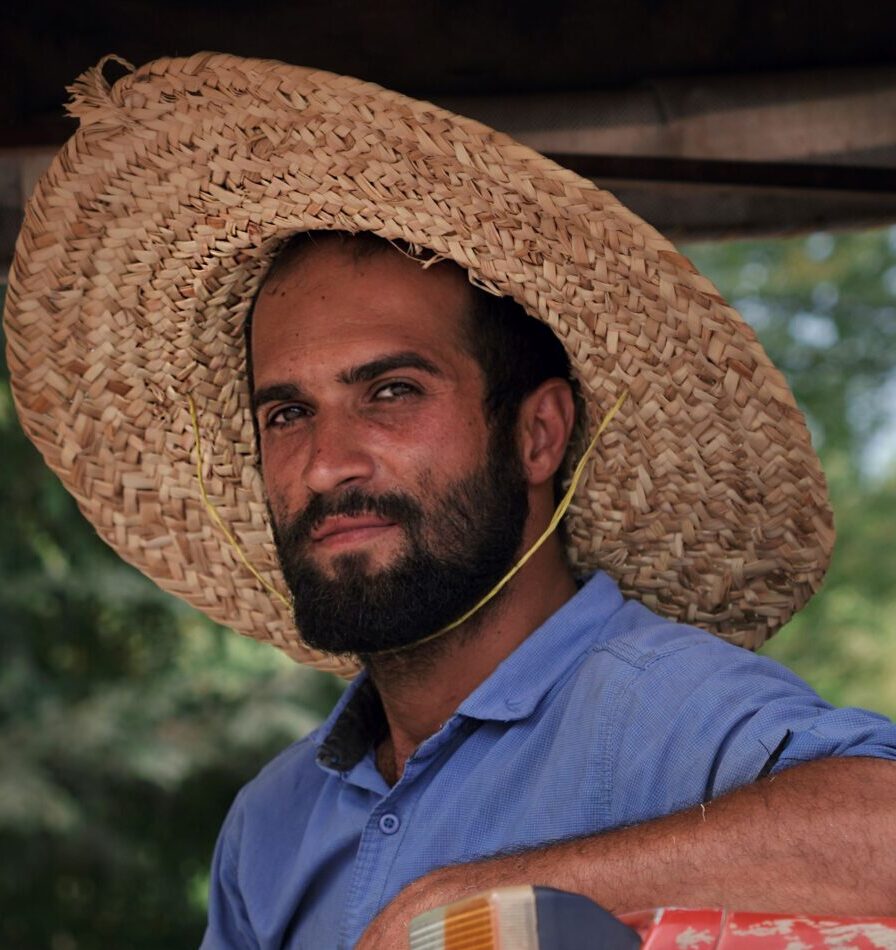 Testimonials A bearded farmer wearing a straw hat smiles while sitting in a tractor outdoors.